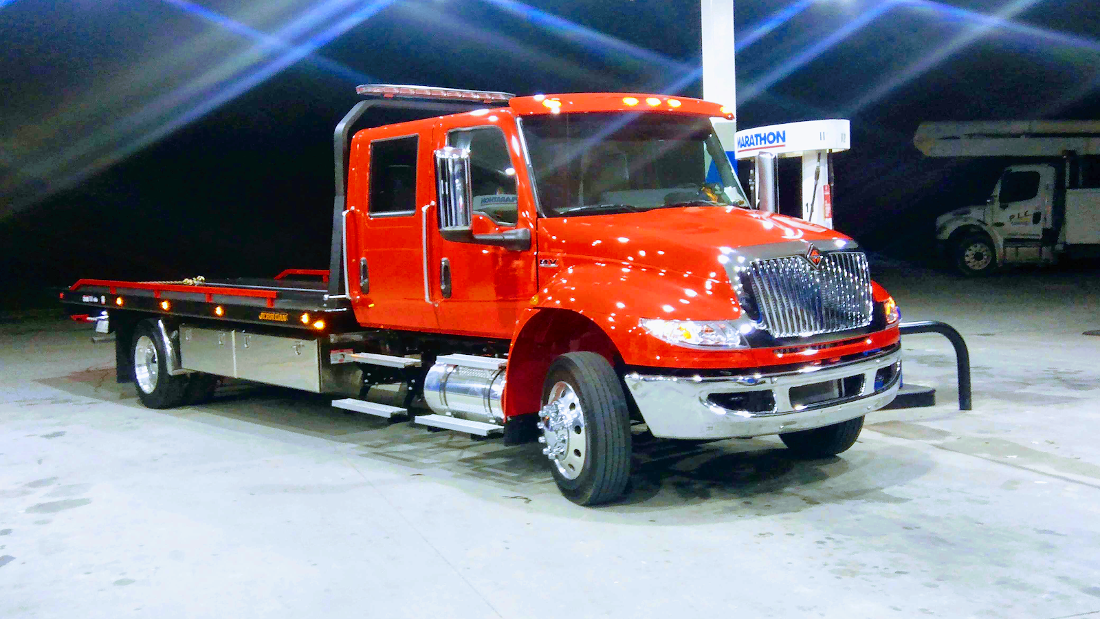 Bright red flatbed tow truck under station lights at night